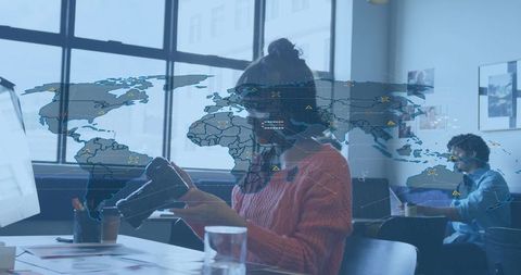 Asian woman holding vr headset coworking desk, wearing rust sweater and glasses, world map overlay