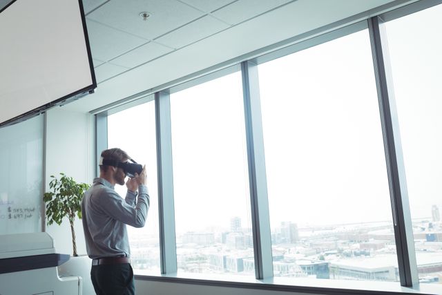 Businessman using virtual reality glasses while standing by glass window at office