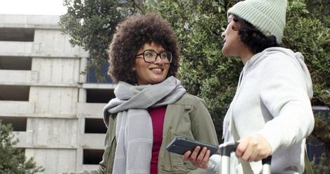 Diverse young women chatting with luggage and smartphone outside urban parking garage