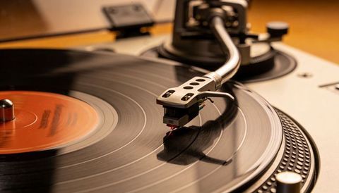Turntable tonearm spinning on vinyl record tracing grooves with amber glow, orange label