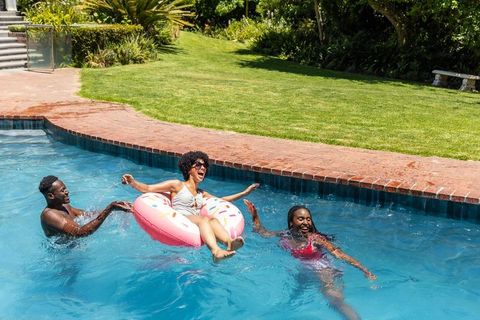 Friends laughing and relaxing on pink donut float in sunny backyard pool