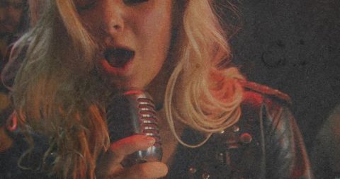 Moody blonde singer holding vintage chrome microphone wearing studded leather jacket
