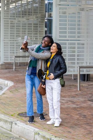 Young diverse couple taking selfie with skateboard on urban brick sidewalk, casual streetstyle