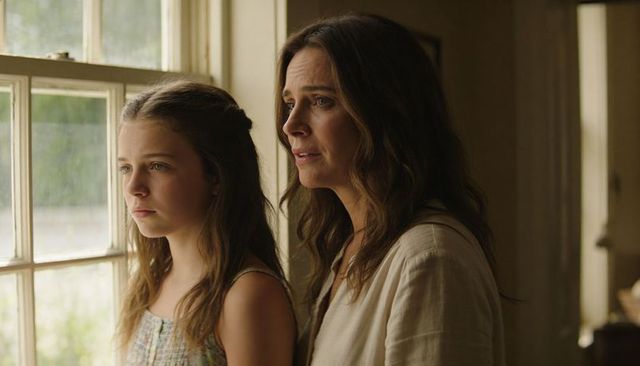 Mother and daughter gazing through sunlit multi-pane window, contemplative family moment