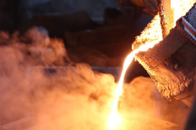 Close-up of molten metal being poured into molds in a foundry, demonstrating industrial metalworking. Useful for illustrating heavy industry processes, manufacturing, and construction themes in educational materials, industrial marketing, and safety training programs.