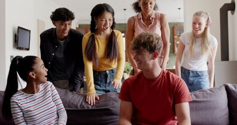 Diverse friends laughing together on gray sofa in bright open-plan living room