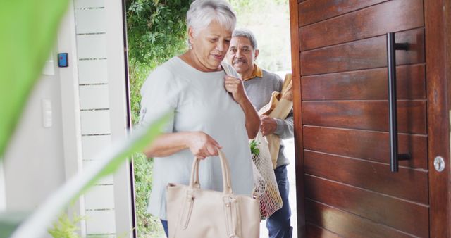 Senior couple entering their home with groceries in eco-friendly reusable bags. The woman is holding a tote bag while the man follows with a bag of groceries, symbolizing teamwork and a healthy lifestyle. Ideal for use in promotions for sustainable living, healthy aging, elderly well-being, retirement lifestyle, and eco-friendly products.