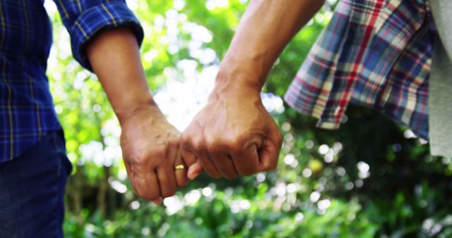 Two people are holding hands, showcasing a bond or relationship, with copy space. Their clasped hands symbolize friendship, support, or partnership against a blurred natural background.