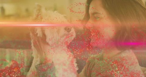 Woman holding fluffy white dog on couch surrounded by warm glittery light and lens flare