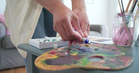 African american artist squeezing blue paint and mixing vibrant palette in home studio