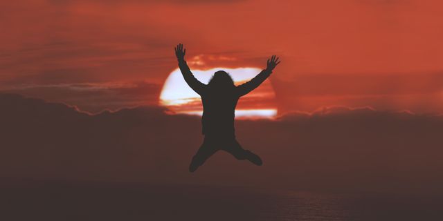 Person jumping with arms raised silhouetted against a bright orange and red sunset sky. This image can be used to represent concepts of freedom, energy, and joy. Ideal for use in inspirational materials, motivational posters, adventure travel promotions, and lifestyle blogs.
