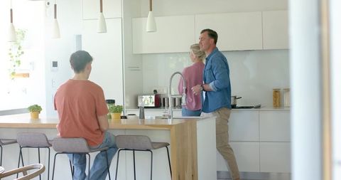 Family morning routine in modern kitchen teen sitting at wooden island parents chatting