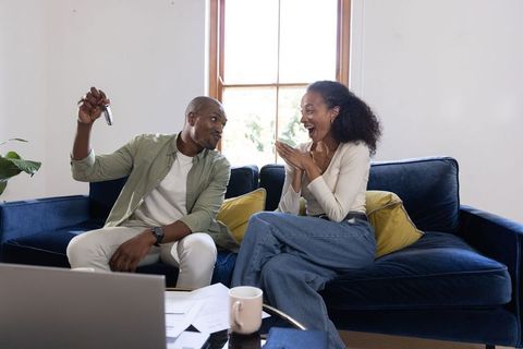 African american couple celebrating new home holding keys on navy blue sofa in living room