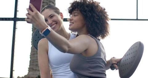 Smiling multiracial women taking gym selfie while holding balance discs and smartwatches