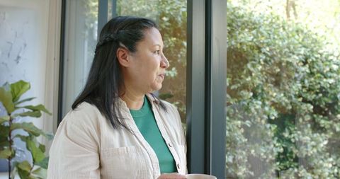Serene african american woman looking out window holding coffee mug in home interior