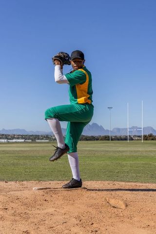 Baseball pitcher preparing to pitch executing windup in green and yellow uniform on mound
