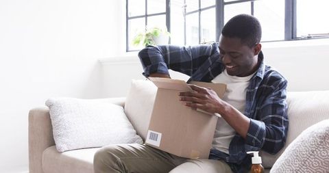 Man on sofa excitedly unboxing parcel in modern living room
