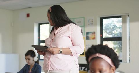 African american teacher holding tablet guiding elementary students in bright classroom
