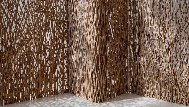 Woven rattan lattice panels and central column casting sculptural shadows on minimal floor