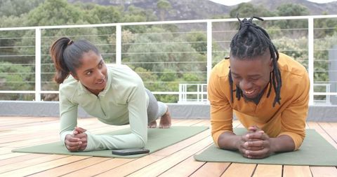 Couple doing forearm plank on rooftop deck with green mats and nature view