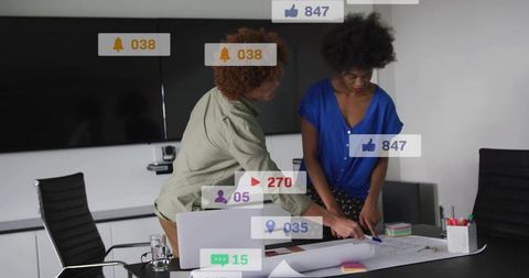 Business team collaborating over blueprint in modern boardroom with rising social pings