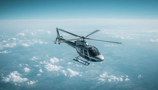Metallic gray helicopter cruising above clouds showing spinning rotors and skid gear