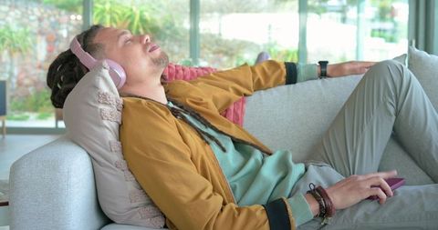 Man relaxing on sofa with pink headphones and smartphone in sunlit modern living room