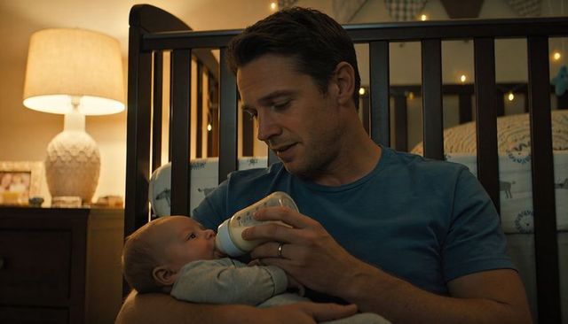 Father feeding infant bottle while cradling newborn in cozy nursery at night