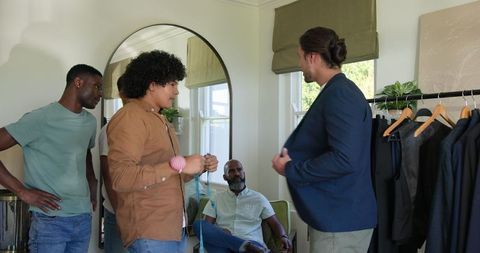 Tailor and groom fitting suit with friends observing in chic room