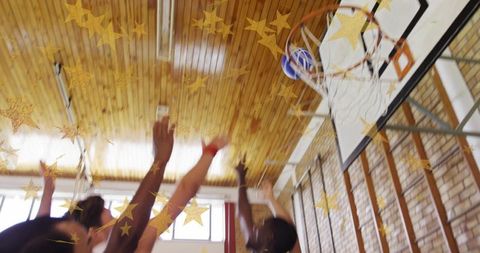 Male basketball players jumping and reaching for ball at hoop with gold star overlay