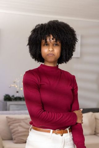Confident woman wearing maroon turtleneck standing in modern living room portrait