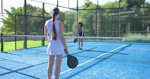 Women playing padel on blue court with glass enclosure and round rackets
