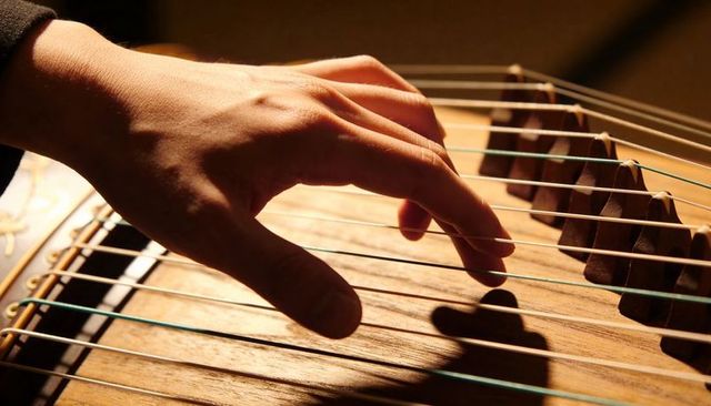 Hand plucking zither strings over movable bridges warm woodgrain closeup