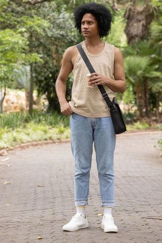 African american man standing in park holding coffee and crossbody bag casual denim look