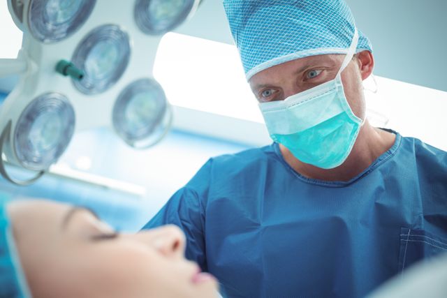 This stock photo captures a male surgeon focusing intensely while performing an operation in a hospital's operation theater. This image is ideal for use in healthcare and medical-themed publications, websites, and educational materials. Suitable for illustrating articles on surgery, healthcare services, medical procedures, and the importance of sterilization in surgical environments. Perfect for promoting hospitals, medical institutions, and health awareness campaigns.