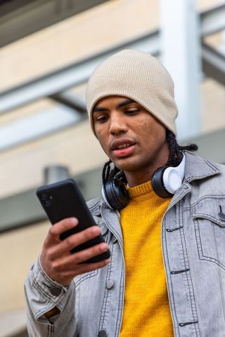 African american commuter checking smartphone at bus stop with beanie and headphones
