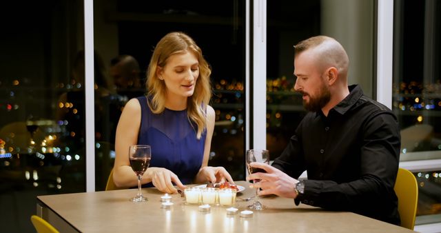 A Caucasian couple enjoys a romantic dinner by candlelight, with copy space. Their intimate setting with a cityscape backdrop creates a cozy and elegant atmosphere.