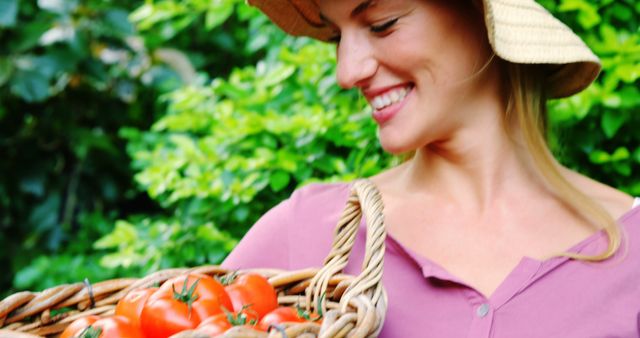 A woman in a garden smiling while holding a woven basket full of ripe, fresh tomatoes. Perfect for use in concepts related to organic farming, healthy lifestyle, sustainable living, gardening activities, and local food production. Ideal for illustrating blog posts or advertisements about fresh produce, home gardening tips, or healthy eating.