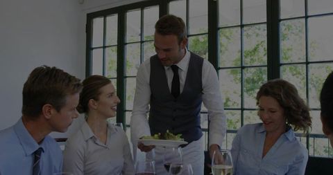 Server presenting plated salad to business lunch group in bright modern restaurant