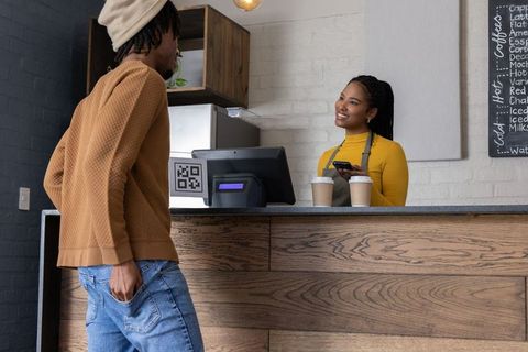 Barista scanning mobile payment while smiling at african american customer in coffee shop
