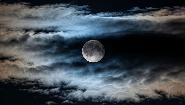 Shining Full Moon Revealing Crater Details through Layered Clouds over Dark Night Sky