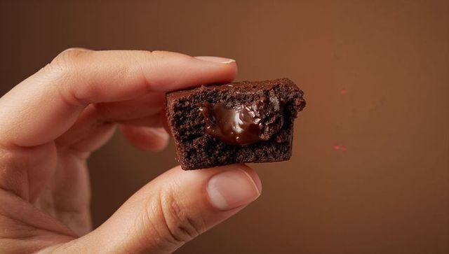 Holding bitten chocolate brownie showing molten center and glossy gooey chocolate filling