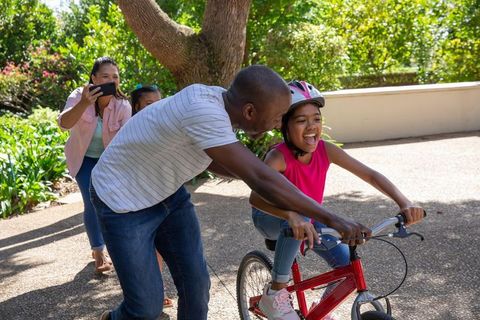 Family Supports Daughter Learning to Ride Bicycle in Sunny Garden