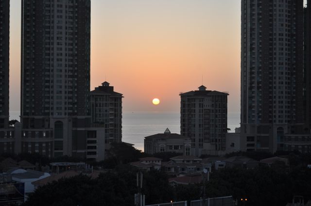 Scenic sunrise over urban high-rise buildings, with the calm sea in the distance. Ideal for blogs and articles on city life, dawn beauty, and tranquil urban scenes. Suitable for travel magazines, real estate advertisements, and websites promoting coastal city living.