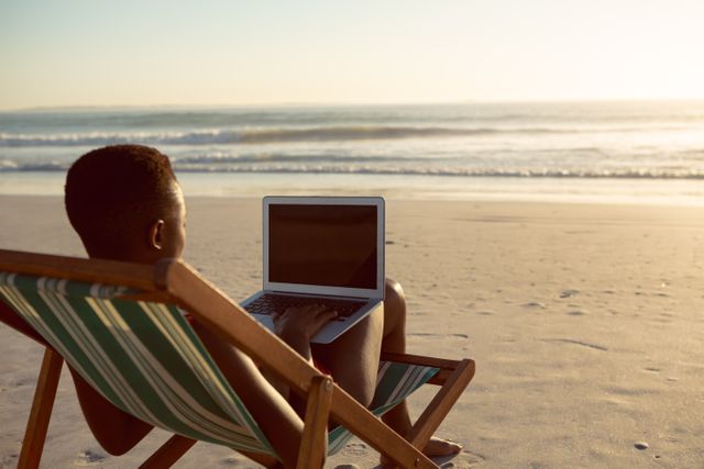 Rear view of woman using laptop while relaxing in a beach chair on the beach