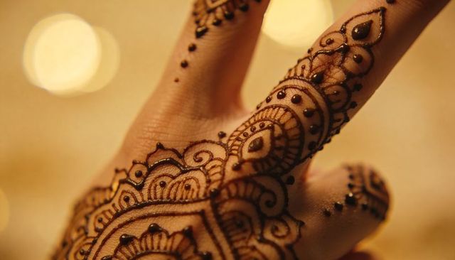 Close-up hand adorning intricate henna mehndi design with paisley floral motifs, bokeh