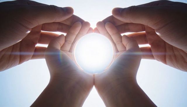Adult and child cupping glowing orb together against bright sky with lens flare