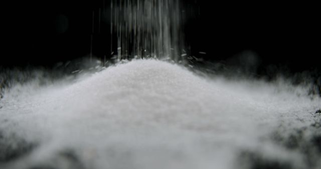 Fine white powder is being poured onto a mound against a dark background, with copy space. The image captures the delicate texture and motion of the powder, suggesting a sense of purity or the process of cooking or baking.