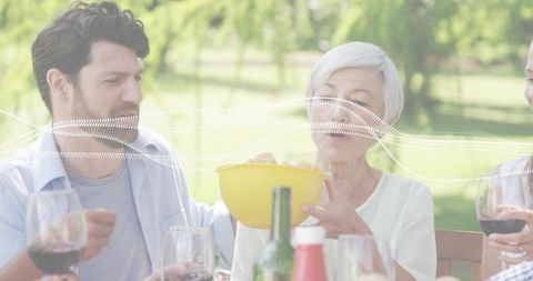 Multigenerational family sharing snacks and wine at sunlit outdoor picnic gathering