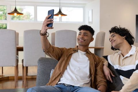 Two friends taking selfie on couch in modern living dining area, smiling casual lifestyle